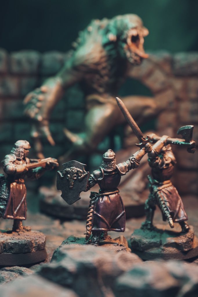 A photograph of miniature models in a dungeon diorama. Three knights are charging into battle against a monster.